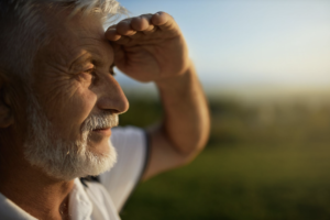 A senior man outside using his hand to block the sun and protect his eyes.